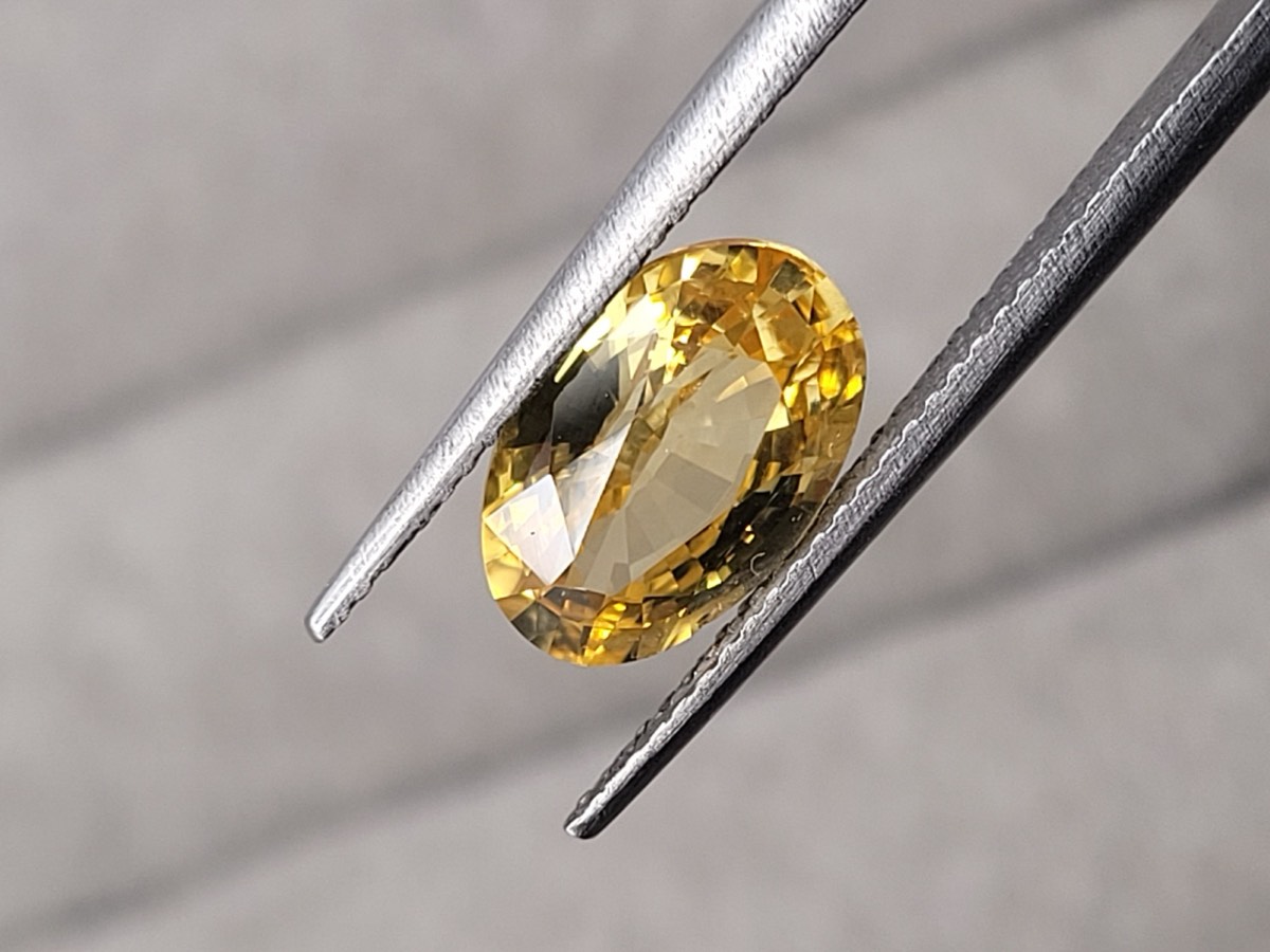 HR17, an unheated 3.01 carat golden yellow sapphire held in tweezers, with faint internal silk visible under the table