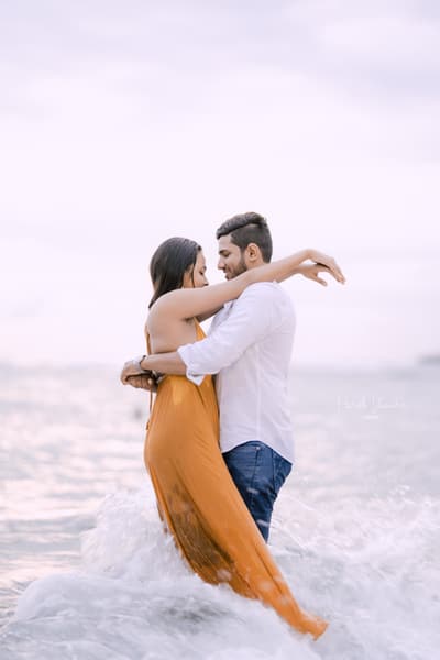 A couple embracing in shallow sea water, her orange saree floating around them.