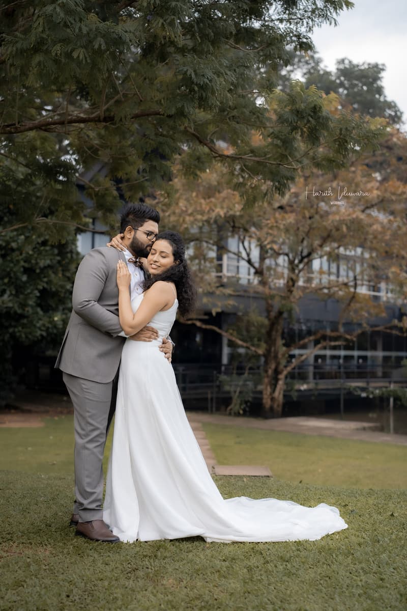 A couple hold each other under a large tree, the bride’s train spread across the grass.